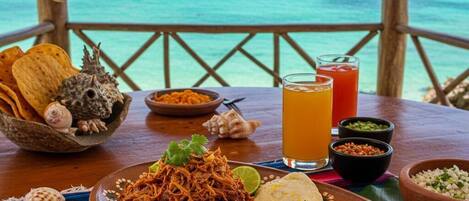 A table with a meal, a drink, and a view of the ocean.