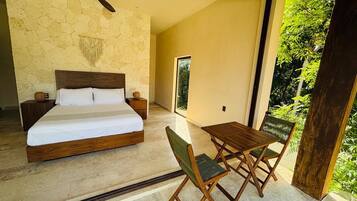 A bedroom with a bed, bedside tables, a ceiling fan, and a view of greenery outside.