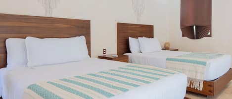 Habitación de hotel con dos camas, cabeceros de madera, ropa de cama blanca y decoración de pared con macramé.