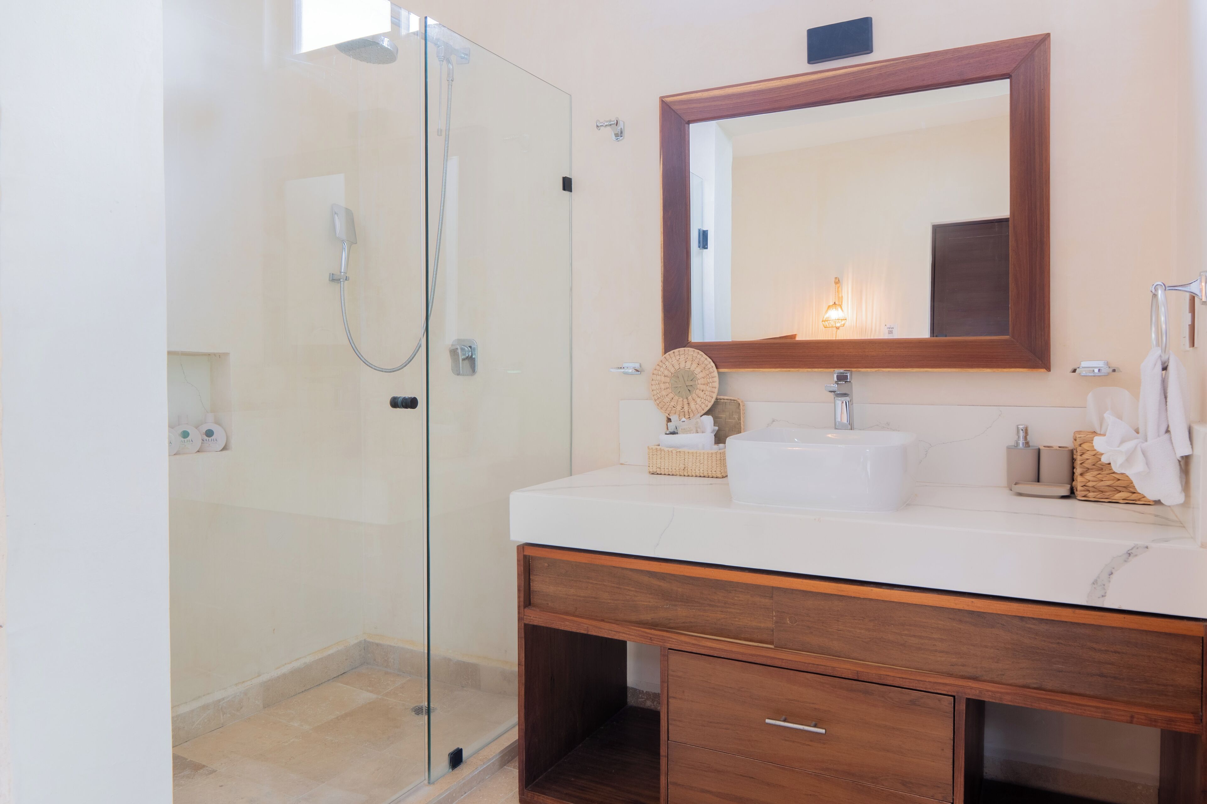 A bathroom with a glass shower enclosure, a wooden vanity with a mirror, and a white sink.