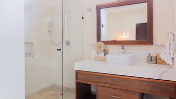 A bathroom with a glass shower enclosure, a wooden vanity with a mirror, and a white sink.