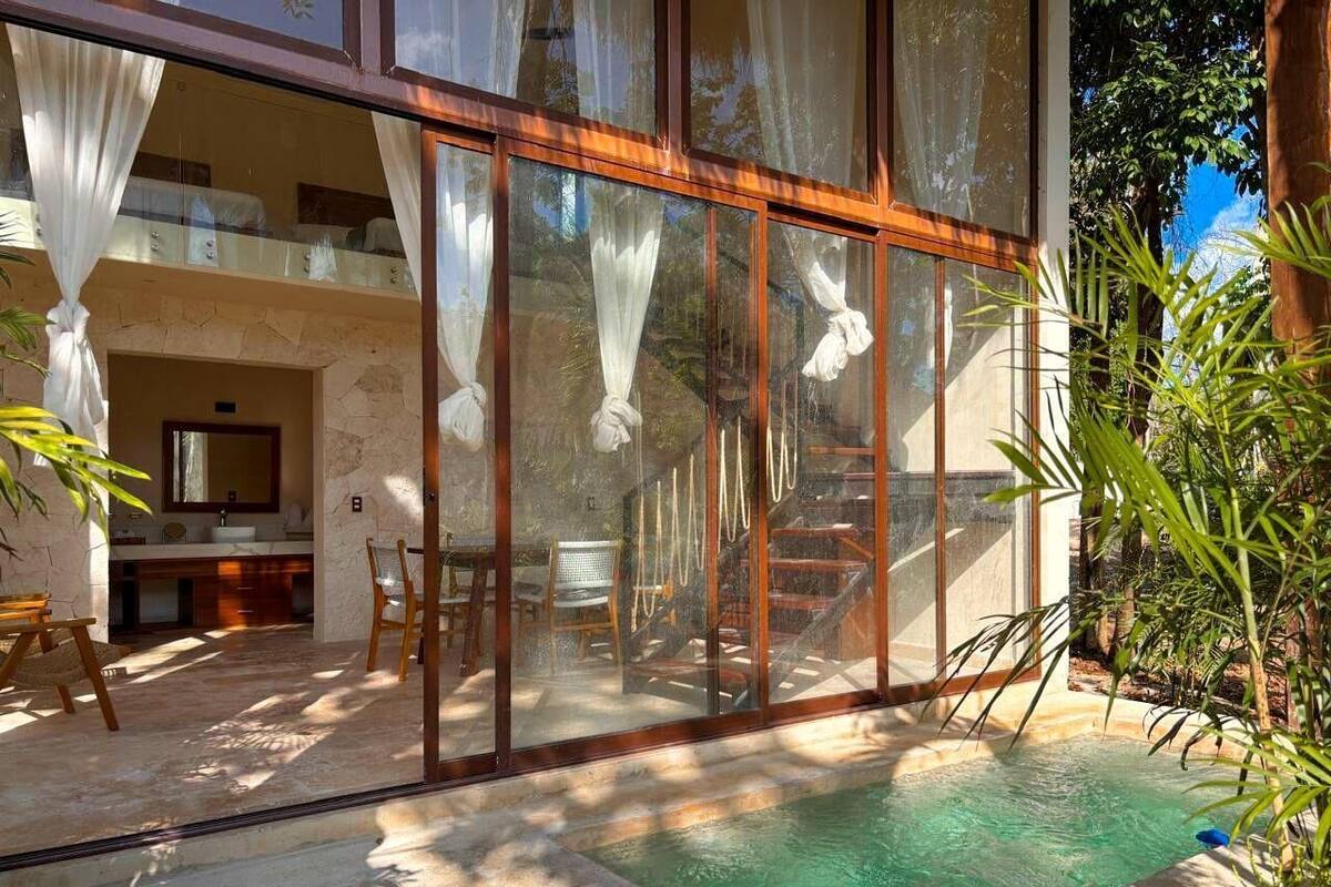 A modern villa with a glass-enclosed swimming pool, a stone fireplace, and a balcony with outdoor furniture.
