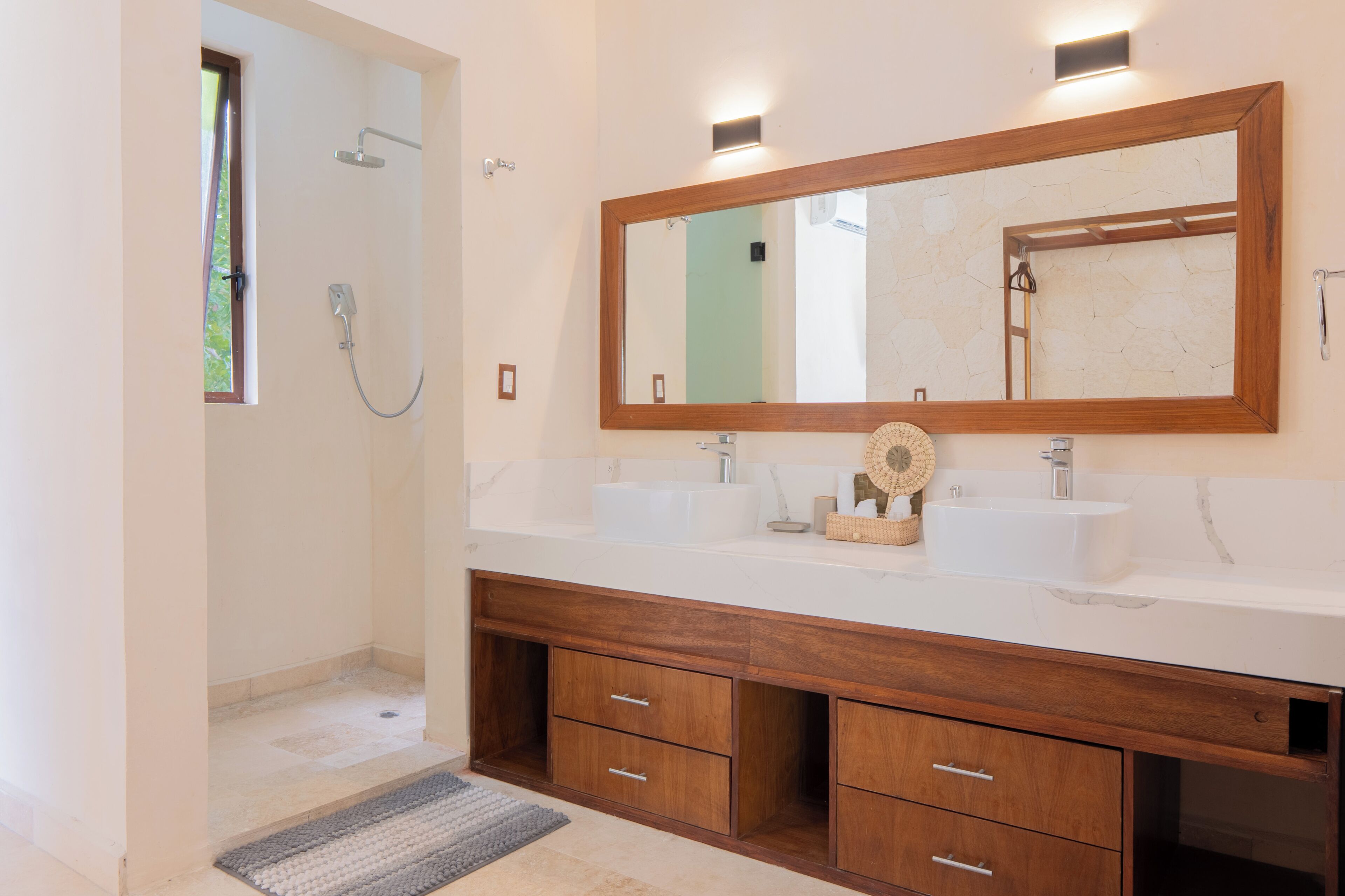 A bathroom with a shower, two sinks, a large mirror, and wooden cabinetry.