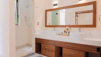 A bathroom with a shower, two sinks, a large mirror, and wooden cabinetry.
