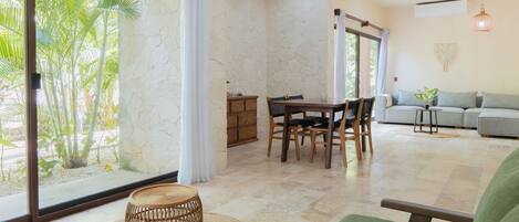 A spacious living area with a dining table, chairs, a sofa, and a large window with curtains.