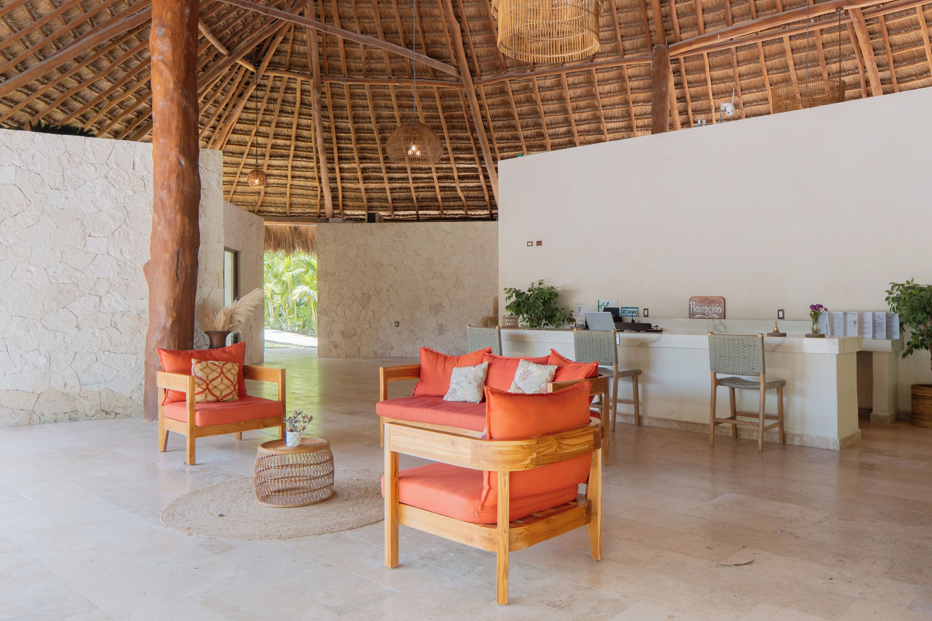 Amplia habitación con techo de paja alto, mostrador de recepción y zona de estar con mobiliario de madera.