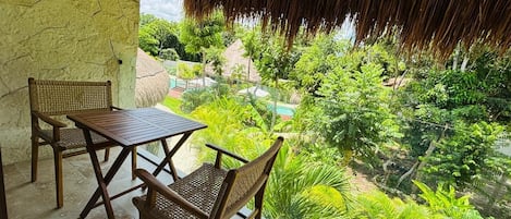 Un balcón con una mesa y sillas, con vistas a un jardín exuberante y una piscina.