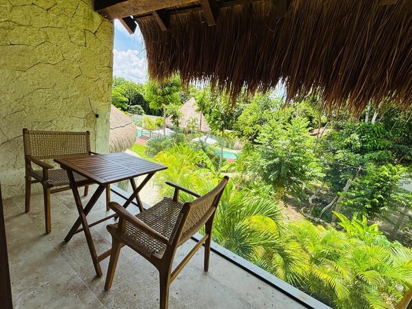 Un balcón con una mesa y sillas, con vistas a un jardín exuberante y una piscina.
