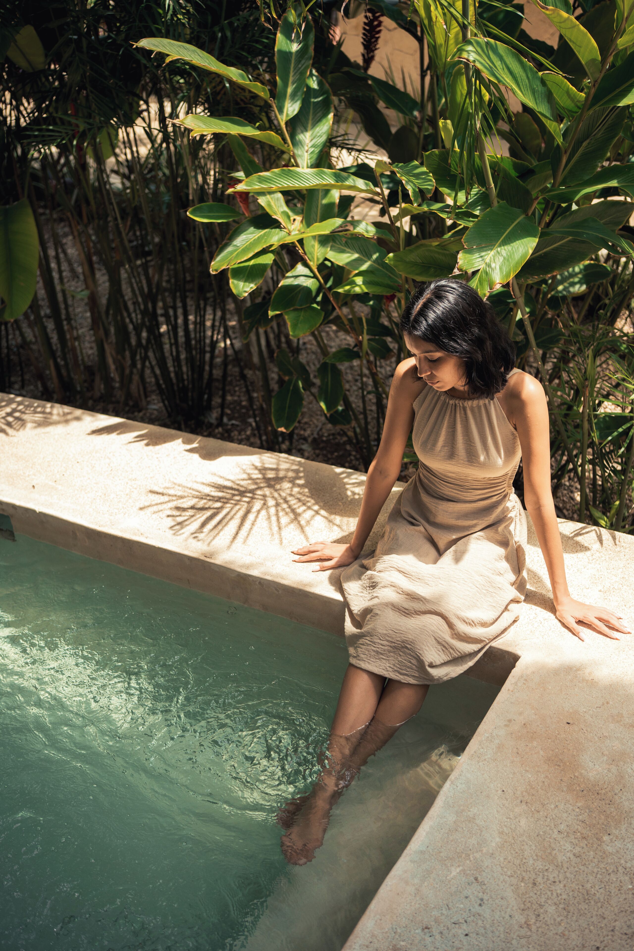 A person sitting by a pool with lush greenery in the background.