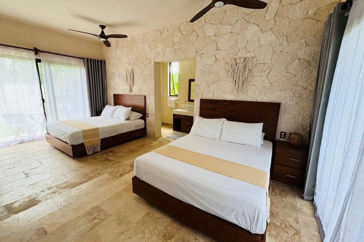 A hotel room with two beds, a stone wall, a ceiling fan, and a view of the outdoors.
