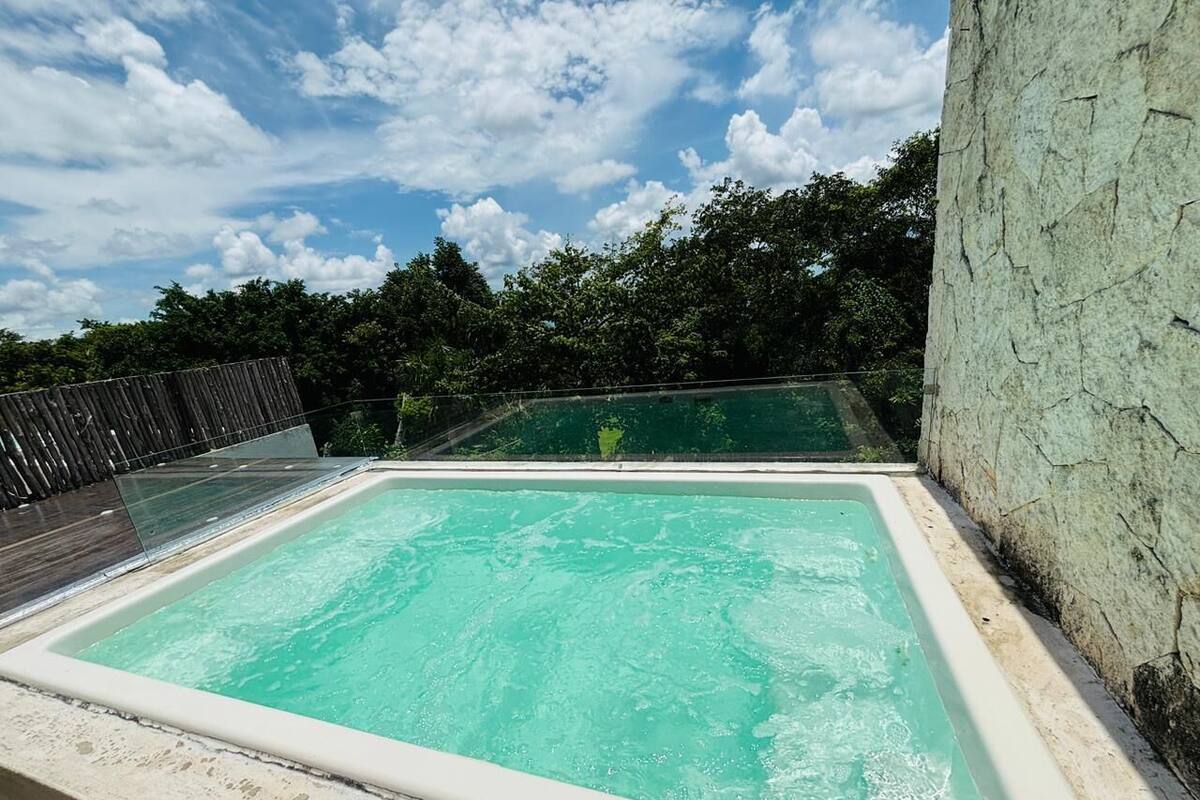 A rectangular outdoor swimming pool with clear water, surrounded by a stone wall and a wooden fence.