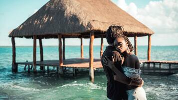A couple embracing on a wooden pier with a thatched-roof structure in the background.