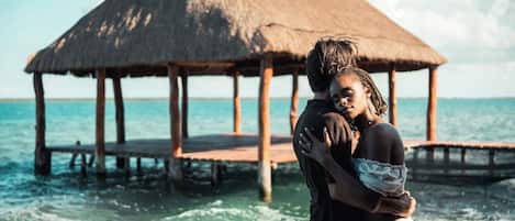 A couple embracing on a wooden pier with a thatched-roof structure in the background.
