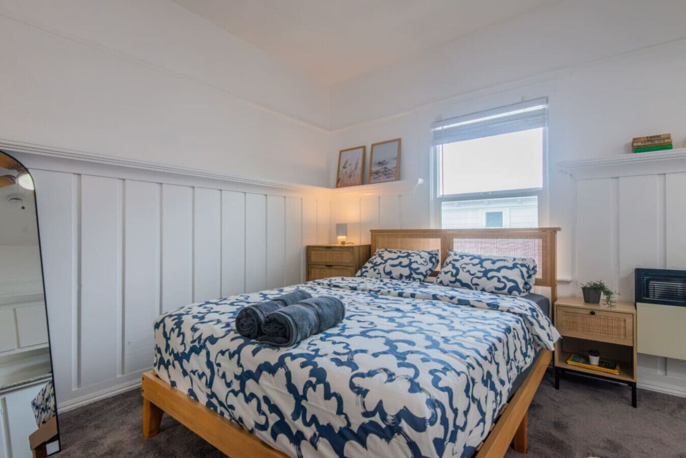 Une chambre à coucher avec un lit, des tables de chevet, un miroir et une fenêtre.