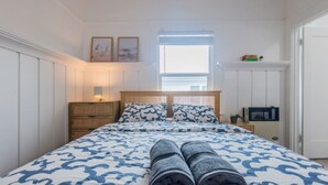 A bedroom with a bed, a nightstand, a lamp, a window with blinds, and a door.