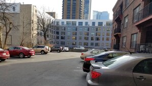 Un parking avec plusieurs voitures, des bâtiments en arrière-plan et un ciel dégagé.