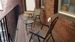 Une terrasse en bois avec deux chaises et une petite table, une porte blanche et un mur en briques.