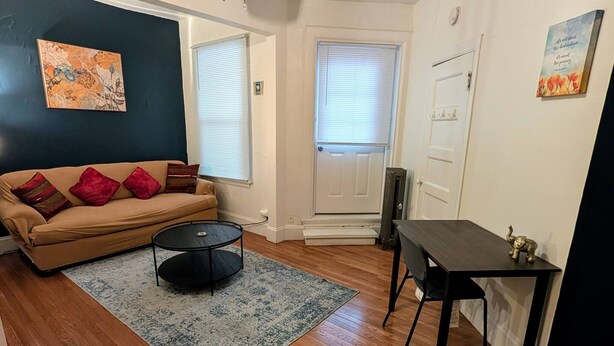 Un salon avec un canapé beige, une table basse ronde, une petite table noire et un tapis à motifs.
