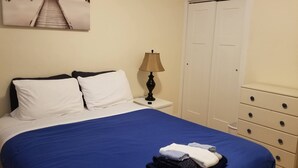 Ein Schlafzimmer mit Bett, Nachttisch, Lampe, Kleiderschrank und einem Bild an der Wand.