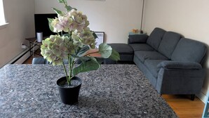 Ein Wohnzimmer mit grauem Sofa, einer Topfpflanze auf einer Granitabdeckung, einem Gemälde an der Wand und einer Lampe.