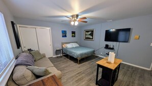 Quarto com cama, sofá, mesa pequena, ventilador de teto, televisão e obras de arte na parede.