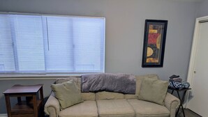 Sala de estar com sofá, uma pequena mesa de madeira, janela com persianas e um quadro na parede.