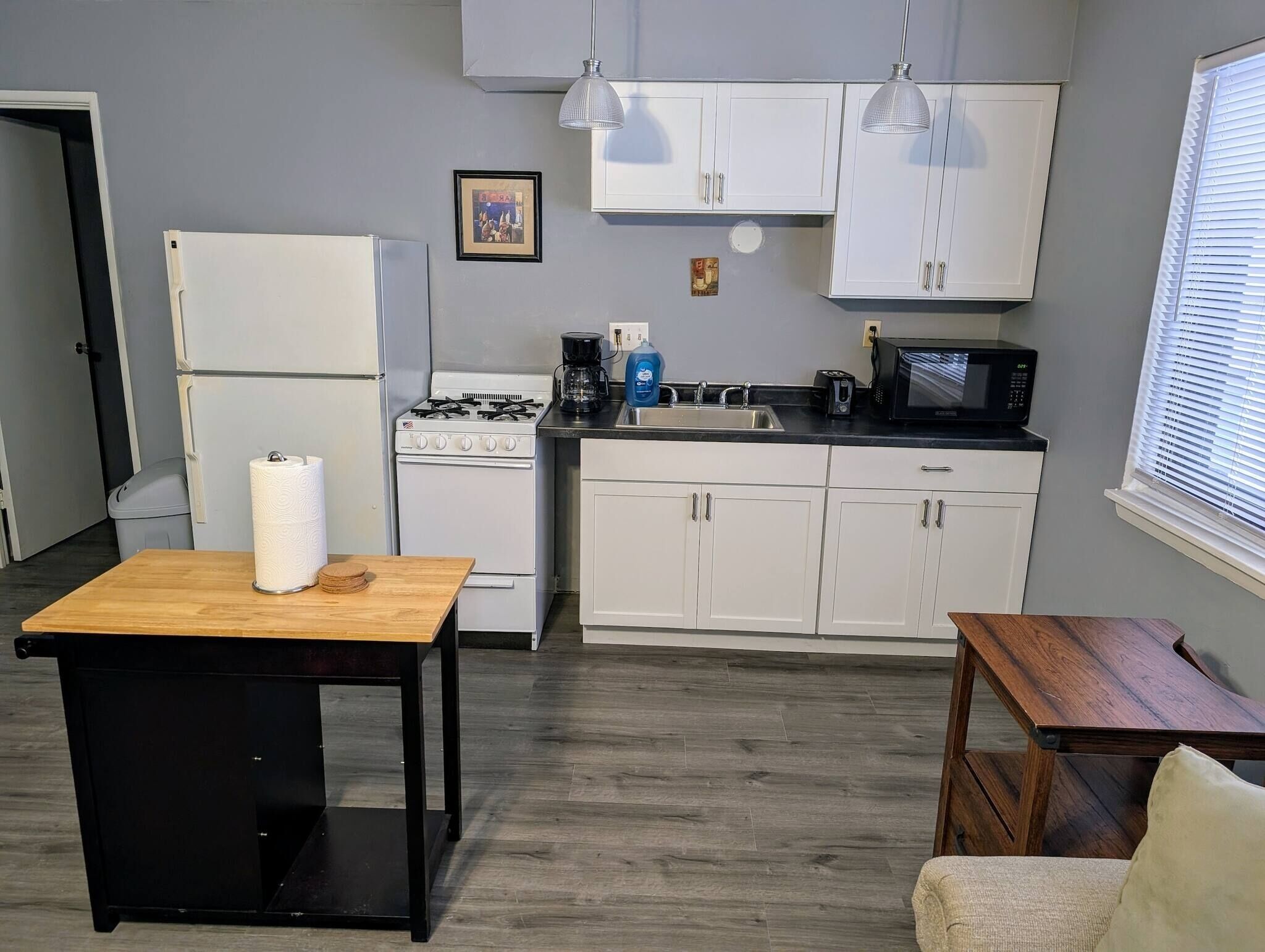 A compact kitchen with white cabinets, a stove, a microwave, and a sink.