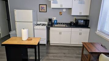 A compact kitchen with white cabinets, a stove, a microwave, and a sink.