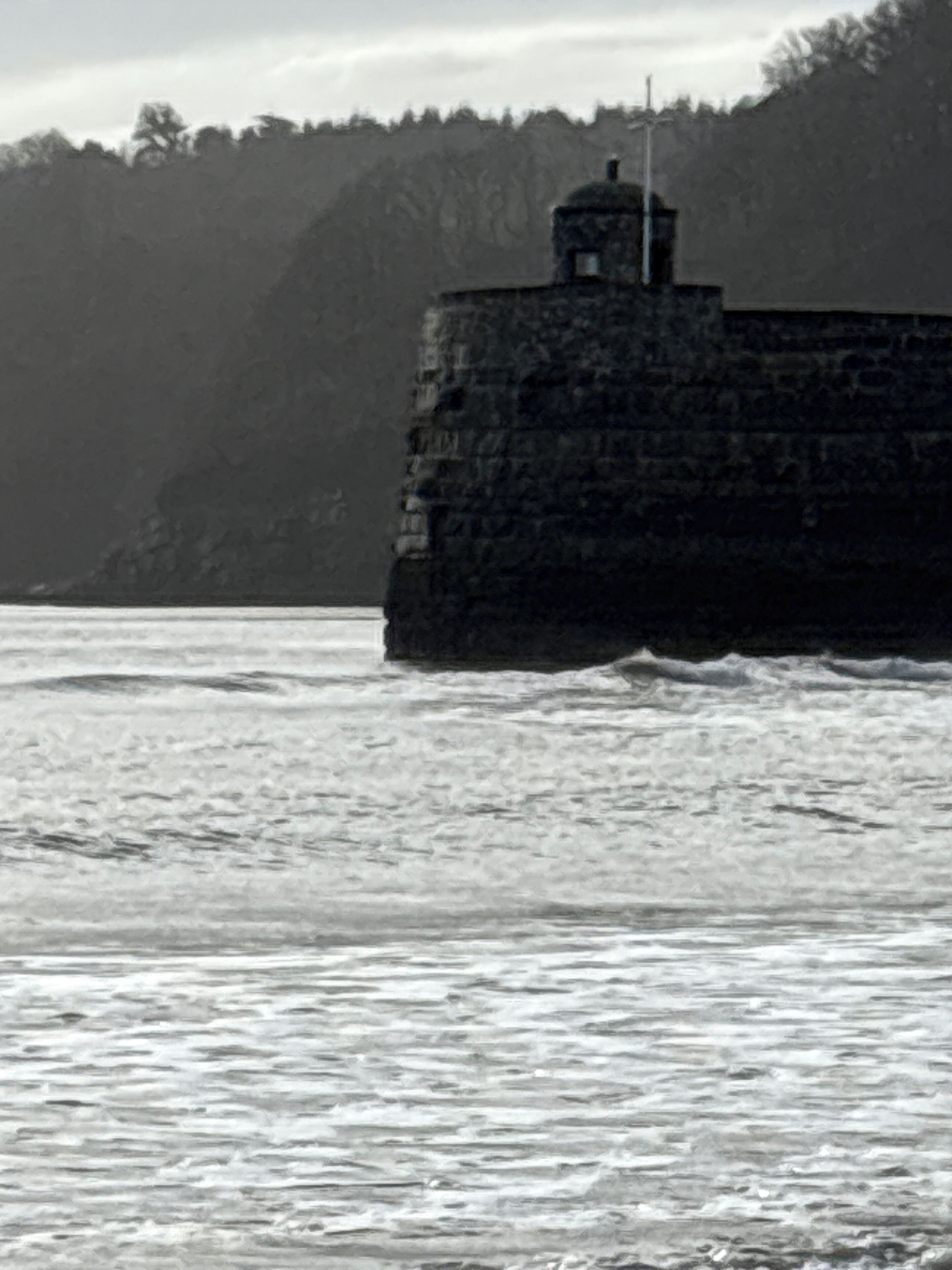 A stone lighthouse by the sea, with waves crashing against its base.