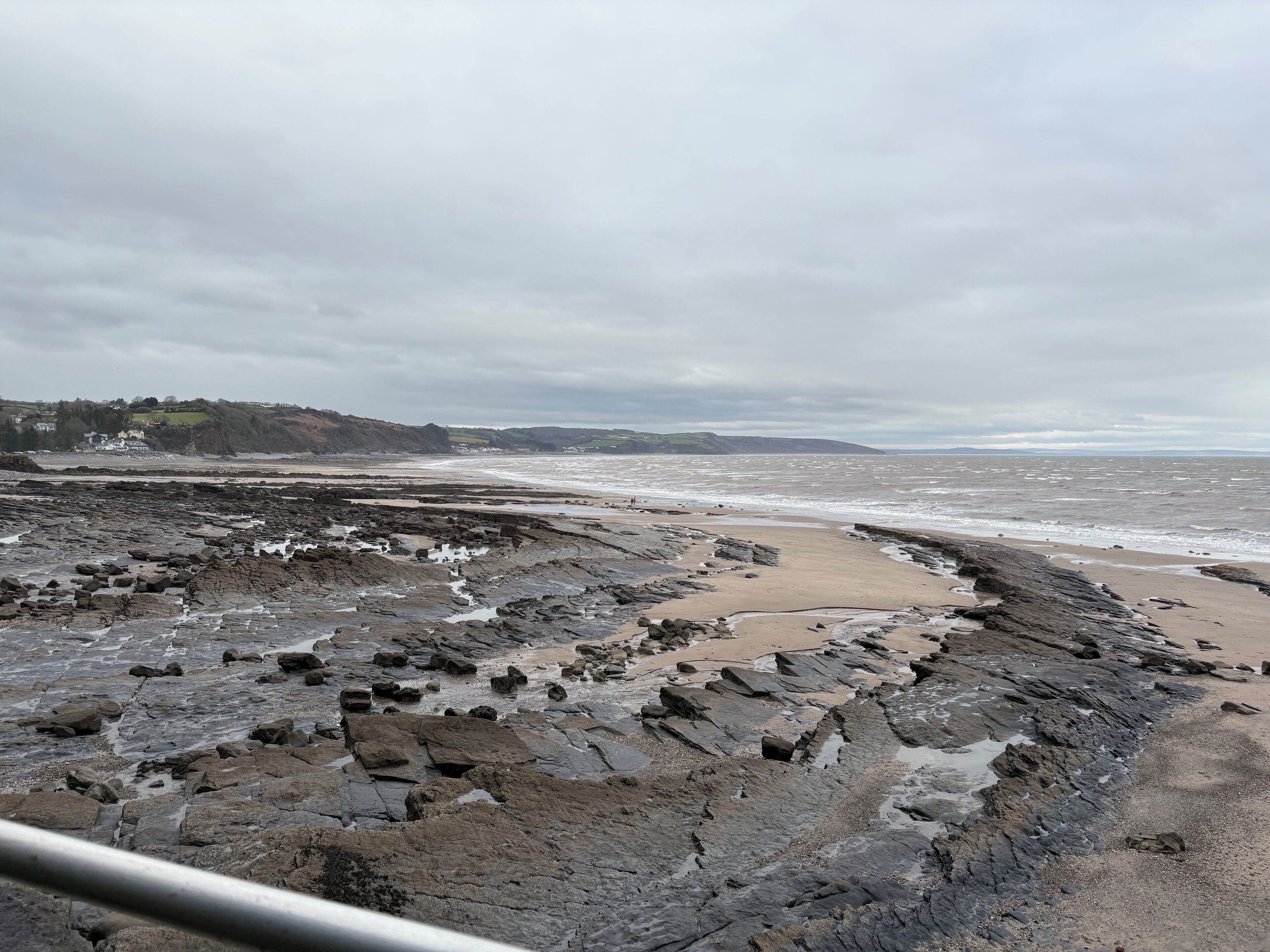 A rocky beach with a view of the sea and distant hills.