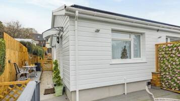 Une maison mobile blanche, dotée d’une petite fenêtre, d’une terrasse en bois et d’un jardin clos.
