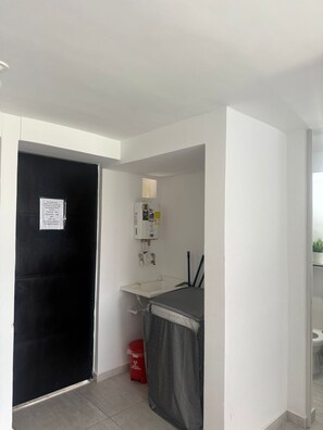 A small, clean bathroom with a white sink, a toilet, and a black door. There is a red trash bin and a white wall with a window.