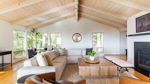 A spacious living room with a high ceiling, large windows, a fireplace, and a cozy seating area.