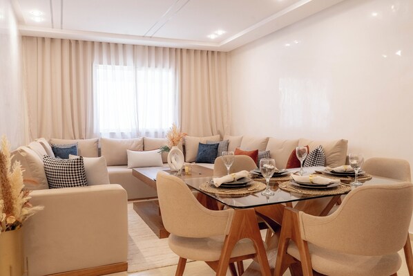 A modern dining area with a glass table, beige chairs, and a sofa with patterned cushions. - Luxury Apartment in Tangier (Tangier)