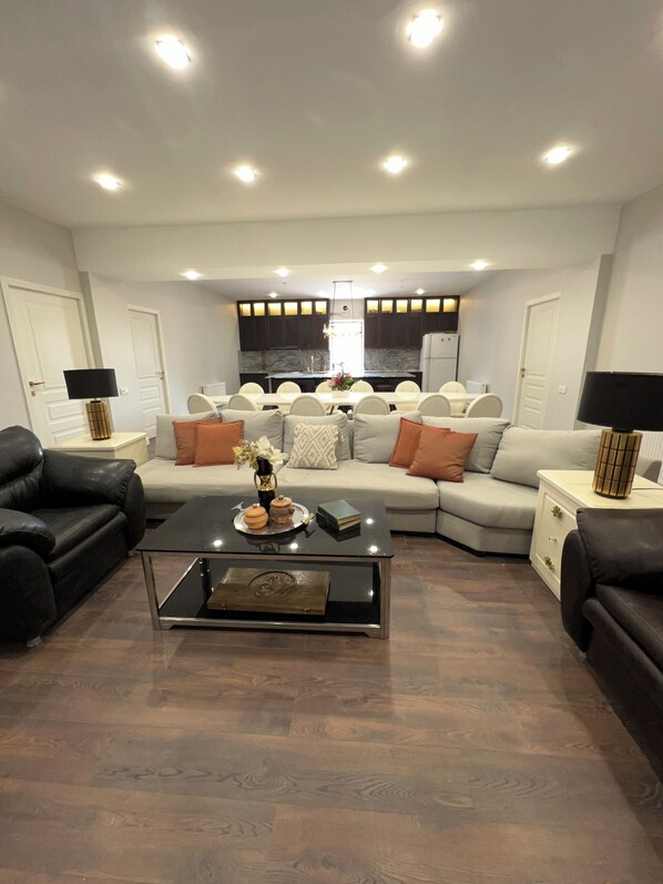 Una sala moderna con un sofá modular, una mesa de centro de vidrio y una cocina al fondo.