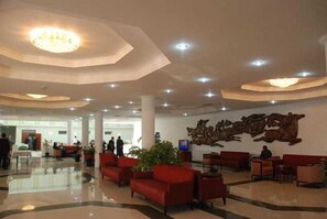 A lobby with a high ceiling, recessed lighting, red seating, and a large wall-mounted sculpture. - Grand Bukhara (Bukhara)
