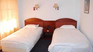 Una habitación de hotel con dos camas individuales, una mesita de noche, una lámpara y una ventana con cortinas.