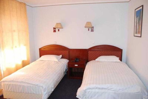 Una habitación de hotel con dos camas individuales, una mesita de noche, una lámpara y una ventana con cortinas.