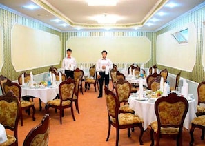 Un salón de banquetes con mesas redondas, sillas y dos camareros.
