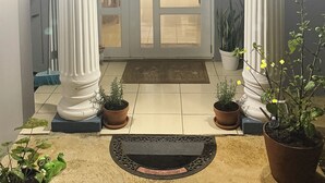A foyer with a double door, two columns, a light fixture above the door, and potted plants.