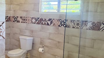 Un baño con dos inodoros, un bidé, una ducha con puerta de vidrio y azulejos estampados.