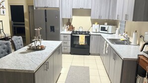 A modern kitchen with grey cabinets, a marble countertop, a gas stove, a microwave, and a refrigerator.