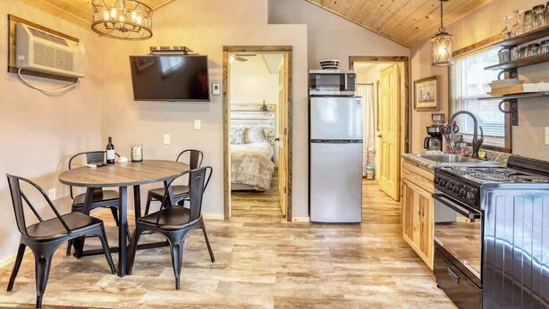 A compact kitchen with a stove, microwave, and refrigerator. There is a dining area with a table and chairs.