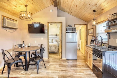 A compact kitchen with a stove, microwave, and refrigerator. There is a dining area with a table and chairs.