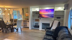 Ein Wohnzimmer mit Kamin, Fernseher, Essbereich und einer Couch.
