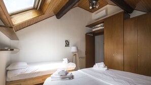A bedroom with two beds, wooden beams, a skylight, and a wardrobe.