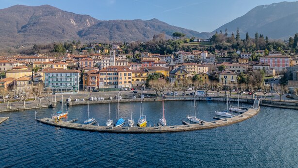 A marina with boats docked, surrounded by colorful buildings and mountains in the background.