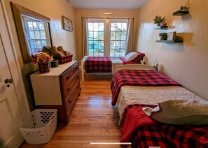A room with two beds, a dresser, a window with curtains, and a view of the outside.