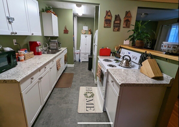 A kitchen with white cabinets, a stove, a sink, and a countertop with various appliances and items.