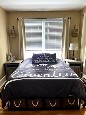 Un dormitorio con cama, dos mesitas de noche, una lámpara y una ventana con persianas.
